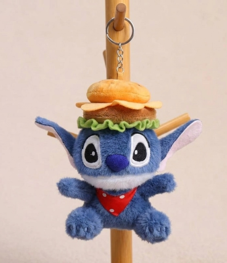 Blue plush toy with a hamburger keychain attached, hanging on a wooden stick against a beige background.