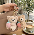 Two teddy bear keychains on a handbag with a cup of coffee in the background