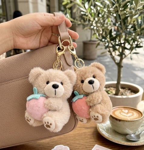 Two teddy bear keychains on a handbag with a cup of coffee in the background