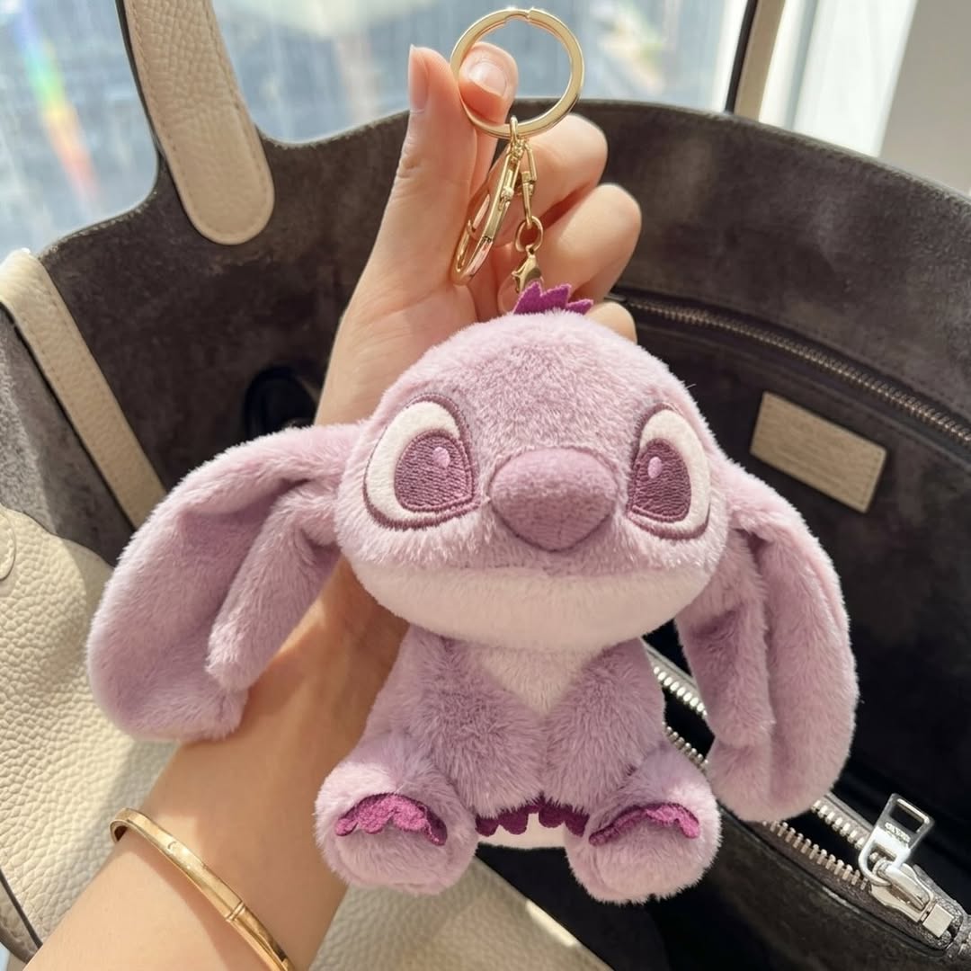 Plush keychain shaped like a cartoon character held by a hand in front of a bag.