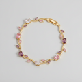 Gold bracelet with pink and clear gemstones on a beige background