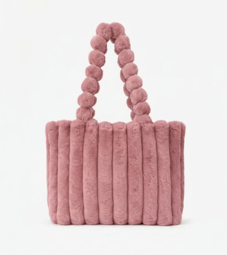 Pink fluffy handbag with pom-pom handle on a white background