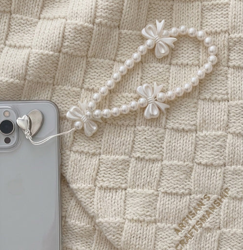 Pearl phone strap with floral designs on a smartphone against a textured beige background