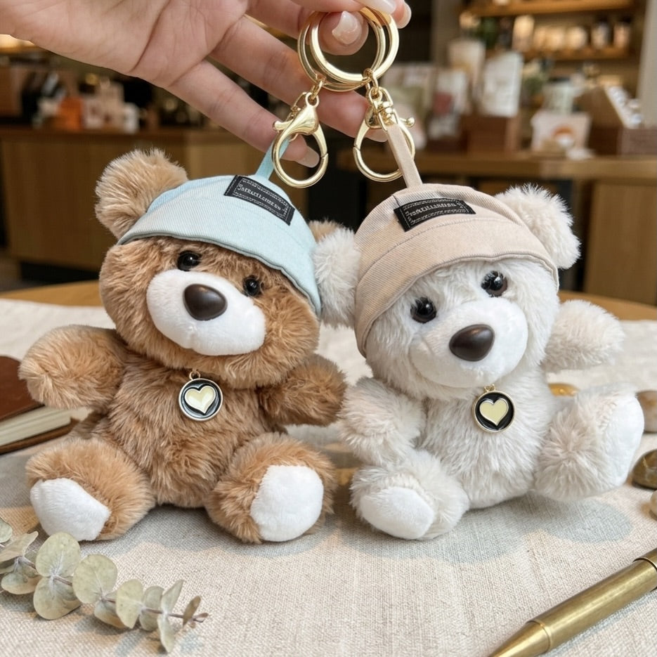 Two teddy bear keychains with hats on a textured surface.
