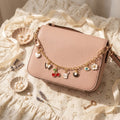 Pink handbag with charm details on a decorative surface with flowers and jewelry.
