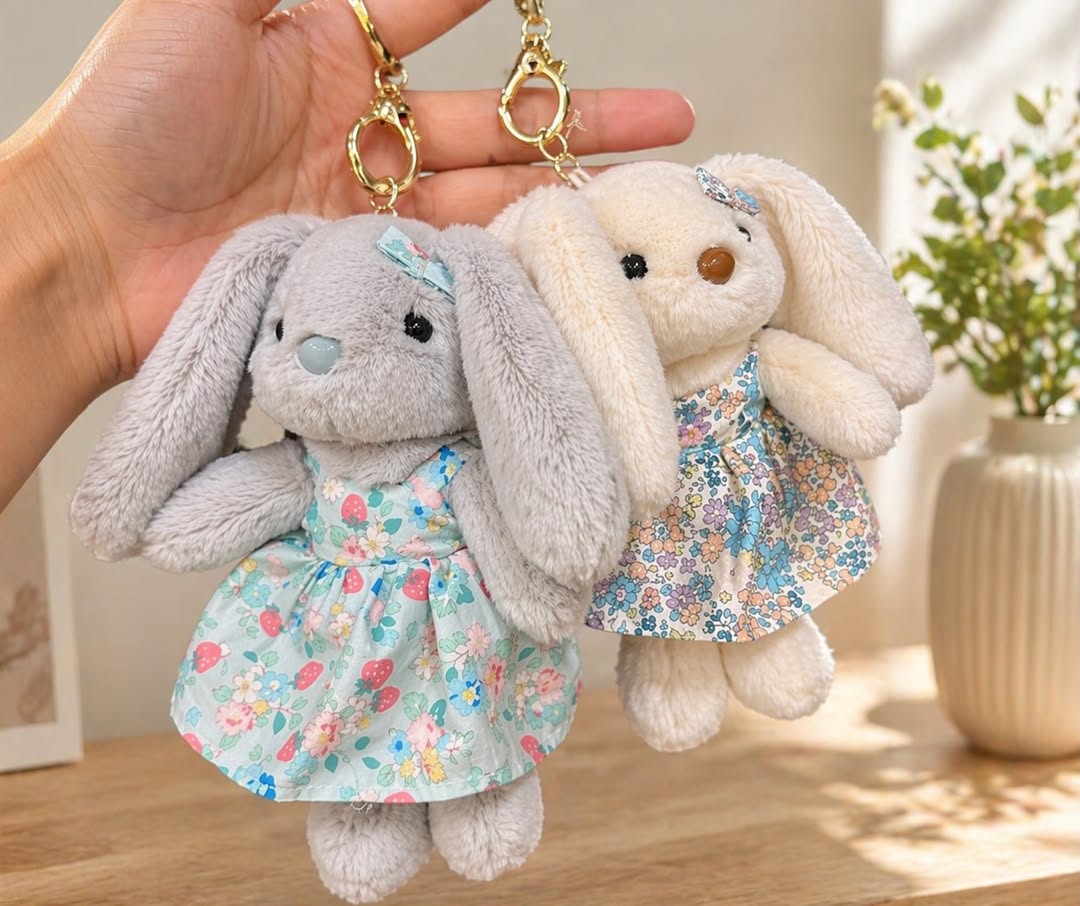 Two plush bunny keychains with floral dresses held by a hand against a neutral background.