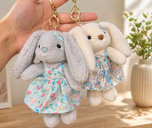 Two plush bunny keychains with floral dresses held by a hand against a neutral background.